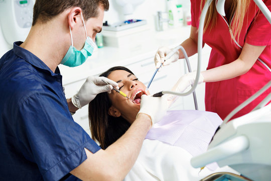 Concentrate dentist and his assistant drilling tooth to female patient on dental chair in dental clinic.