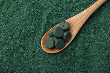 Spoon of spirulina pills on algae green powder, top view with space for text