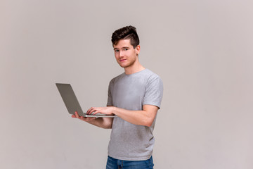 Smiling and laughing handsome young man use and show laptop. isolate. grey t-shirt and blue jeans