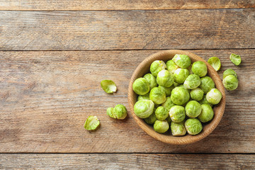 Bowl of fresh Brussels sprouts on wooden background, top view with space for text