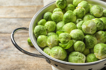 Colander with Brussels sprouts on wooden background, closeup