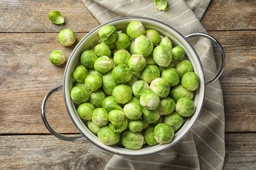 Colander with Brussels sprouts on wooden background, top view