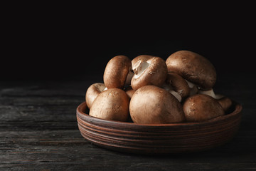Bowl with fresh champignon mushrooms on wooden table. Space for text