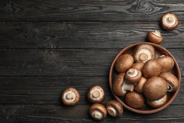 Bowl with fresh champignon mushrooms on wooden table, top view. Space for text