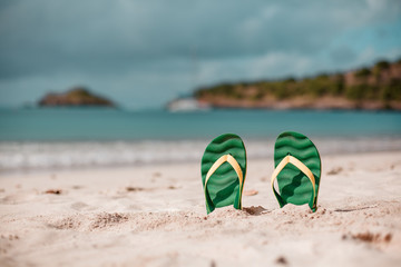 Green flip flops in the white sandy beach near sea waves, nobody. Summer vacation concept with blue...