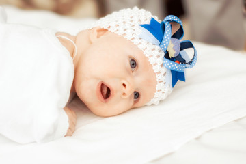 a little baby of two months lies on the bed in a white blouse and a beautiful bandage on her head and smiles with the first smile.