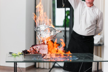 The chef pours alcohol to baked Turkey on a platter in the fire.