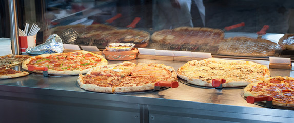 Fresh Italian pizza in pizzeria window in fast food restaurant