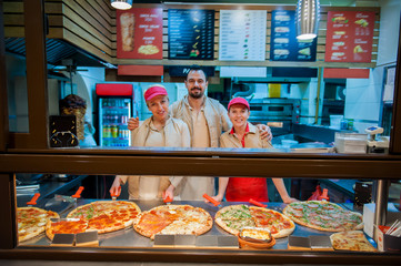 Smiling young stuff aprons selling pizza in fast food restaurant