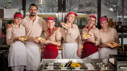 Smiling young stuff aprons selling pizza in fast food restaurant