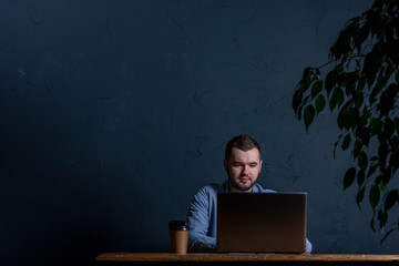 Young businessman working on his laptop on wooden table. Room for text. Dark background. Space for Text