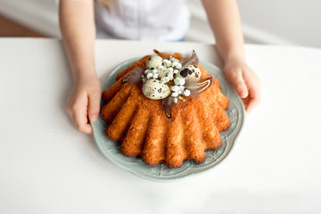 Little girl's hands hold a plate with easter cupcake decorated with easter eggs and feathers. Breakfast