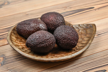 Four ripe brown avocados on wooden carved bowl.
