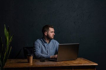 Young businessman working on his laptop on wooden table. Room for text. Dark background. Space for Text