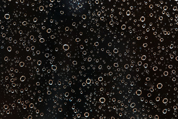 Closeup of rain water drops behind glass at evening. It looks like bubbles in black liquid. Abstract wet background.