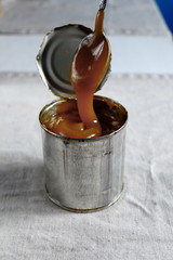  Domashnyaya traditsionnaya varenaya sgushchenka v zhestyanoy banke l'yetsya s lozhki na stole 79/5000 Homemade traditional boiled condensed milk in a tin poured from a spoon on the table