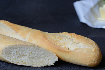 Fresh french roll baked crunchy baguette bread and butter on dark background. Closeup of crust of...