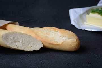 Fresh french roll baked crunchy baguette bread and butter on dark background. Closeup of crust of...