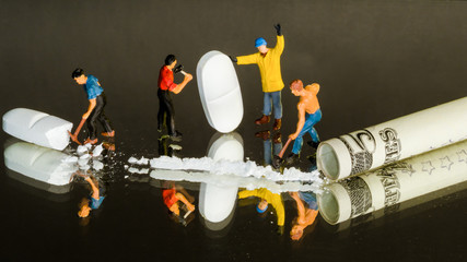 Miniature figures crushing drugs to a line for sniffing with a dollar bill