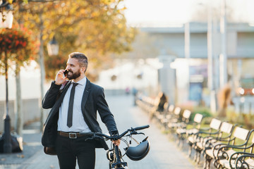 Businessman commuter with bicycle walking home from work in city, using smartphone.