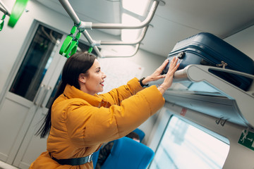 Young female puts luggage on the shelf railway train.