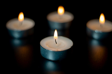 Four tea candles with reflection on black