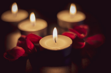 Obraz na płótnie Canvas Four tea candles and rose petals in the dark