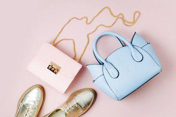 Fashion handbags with shoes on pale pink background. Flat lay, top view. Spring/summer fashion...