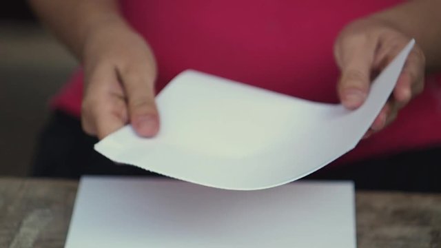 The woman puts the sheet of paper in half. Creative work with paper. Scissor a sheet of paper. Action in air over a wooden table. Close up. Retro style.