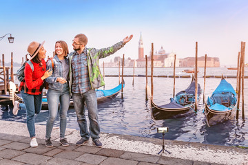 Fototapeta na wymiar Group of happy friends travelers having fun on San Marco Square with gondolas and Grand channel at the background in Venice. Vacation and holidays in Italy and Europe concept