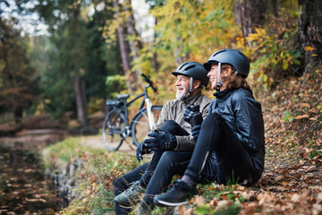 A senior couple with electrobikes sitting outdoors in park in autumn, resting.