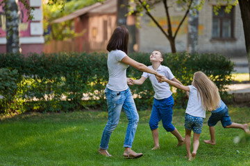 Naklejka na ściany i meble Mother and children dance on the lawn in the park