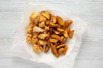 Tasty fastfood: fried potato wedges and chicken bites on a white wooden background, top view. Flat lay, overhead.