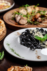 The concept of Italian cuisine. Black pasta with cuttlefish ink, parmesan cheese and basil. Serving dishes in a restaurant in a white plate. copy space