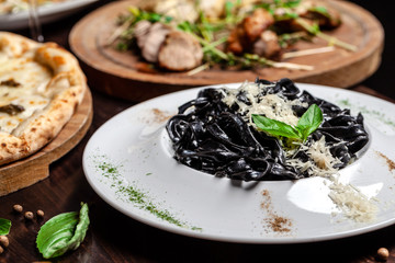 The concept of Italian cuisine. Black pasta with cuttlefish ink, parmesan cheese and basil. Serving dishes in a restaurant in a white plate. copy space