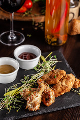 The concept of Italian cuisine. Snack to beer. Glazed chicken legs and chicken wings, breaded. Serving dishes in the restaurant on a black stone slate. Copy space