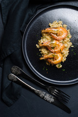 Italian risotto with shrimp on a black plate. Dark background, top view