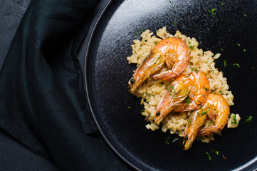 Italian risotto with shrimp on a black plate. Dark background, side view