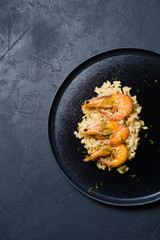 Italian risotto with shrimp on a black plate. Dark background, top view, space for text