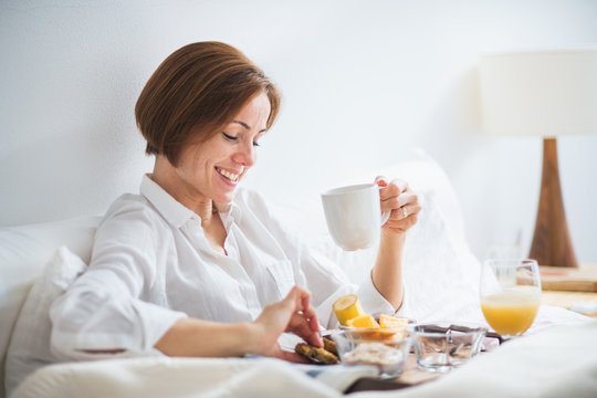 A woman having breakfast in bed in the morning. - Powered by Adobe
