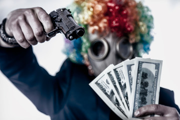 Male gangster in the mask clown with gun takes the money. Criminal concept. Focus on the gun.