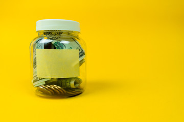 Money jar with coins and paper dollars with sticker for your text, copy space. Isolated on yellow background