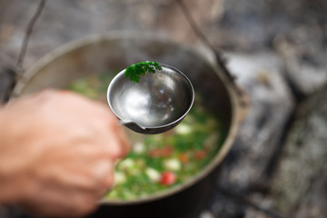 Man hand with metal ladle and soup in cauldron at background