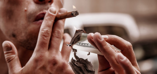 Close up brutal businessman lighting cigar with $100 dollar bill. Selective focus on the mburning...