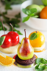 Mousse dessert in the shape of a pear fruit, orange fruit and cherry.