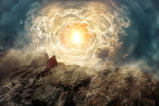 Mann auf einem Felsengipfel schaut in einen surrealen Wolkentunnel