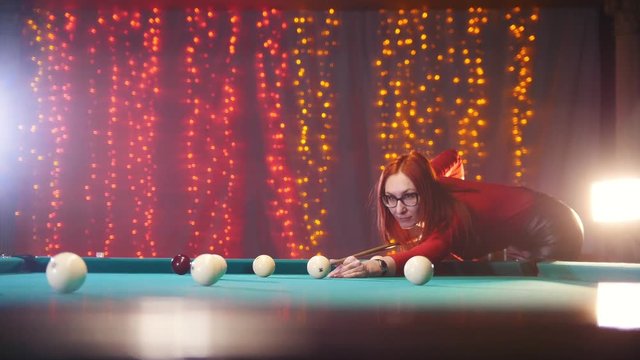Concentrated ginger woman in red turtleneck playing billiard