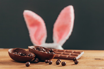 Easter concept. Rabbit ears behind chocolate easter egg on wooden table
