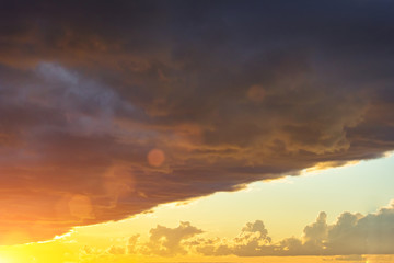 Dark sharp edge of a thundercloud front in front of a sunset sun, bright light.