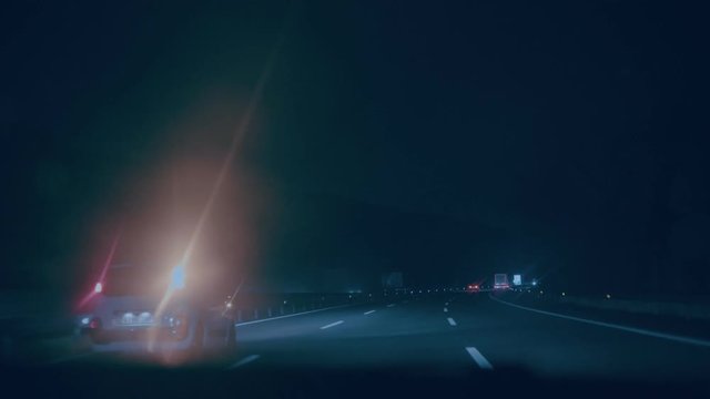 Slow motion stranger things vibes shot of highway at night time, cars move on freeway with stop lights, overtake during after work commute. windscreen washer moves in rain